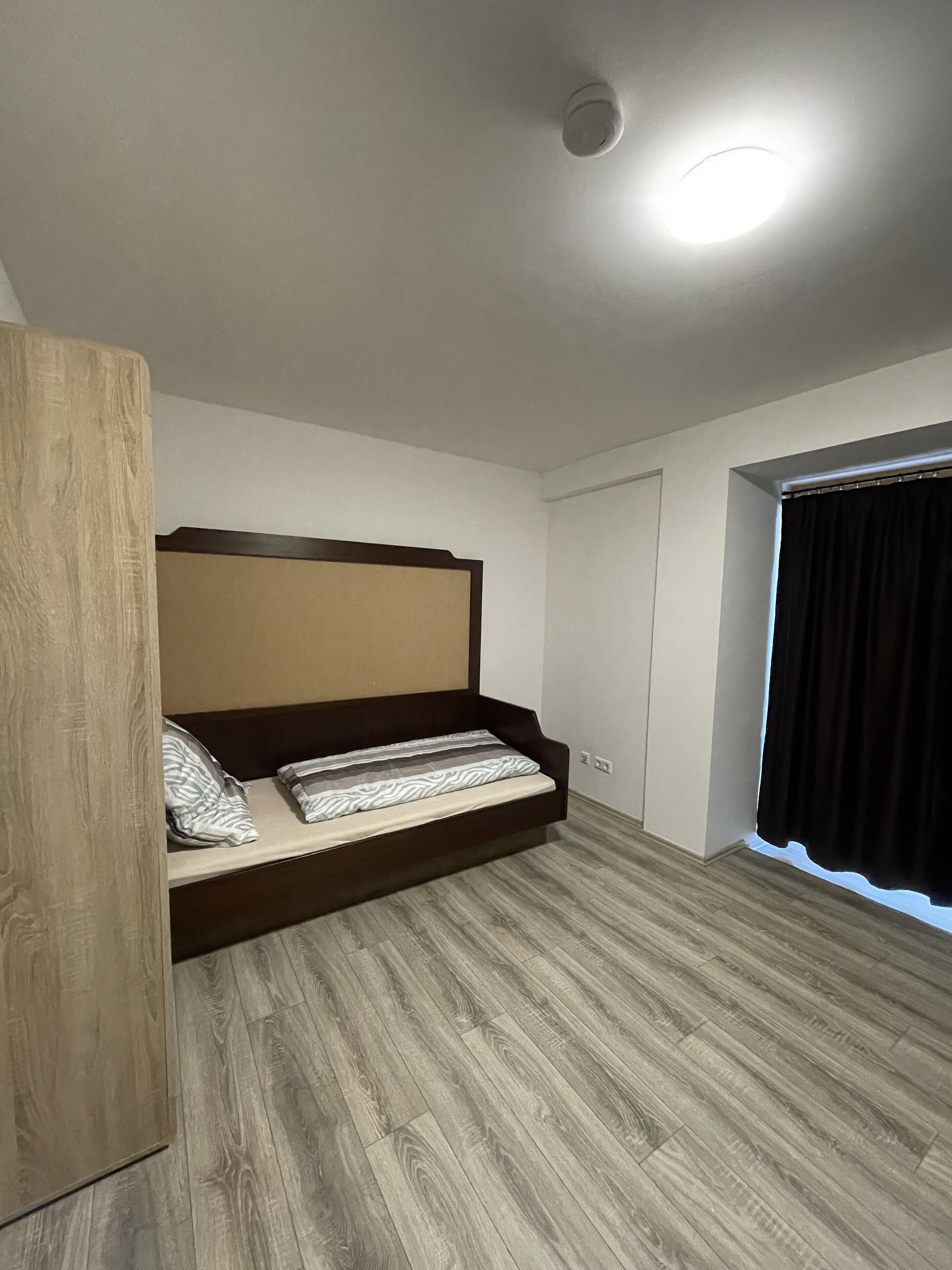 A bedroom with a bed, wooden wardrobe, and a window with curtains.