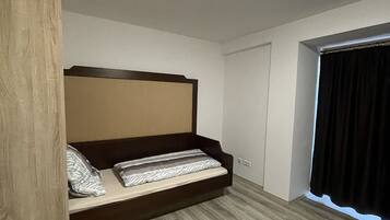 A bedroom with a bed, wooden wardrobe, and a window with curtains.