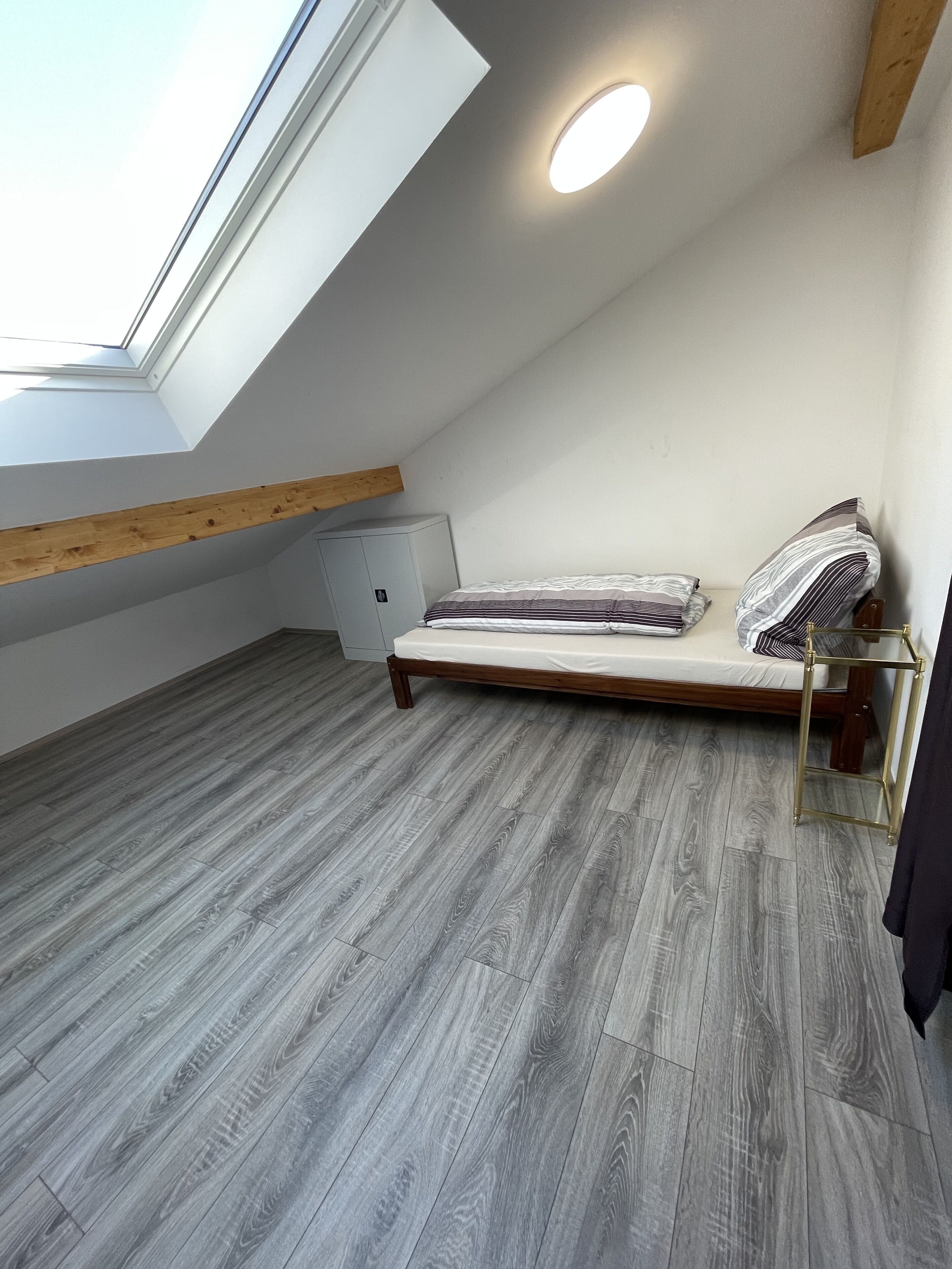 Una habitación con techo inclinado, una cama con estructura de madera, una mesita de noche pequeña y un radiador.