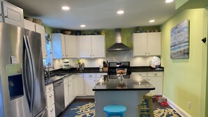 A modern kitchen with white cabinets, stainless steel appliances, a central island, and a blue stool.