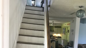 A staircase with white and dark wooden steps leading to a second floor. A wooden handrail is on the left, and a white vase is on the right.