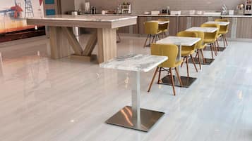 Un hall d'hôtel moderne avec un sol en marbre, un îlot central doté d'un bar, des chaises jaunes et une pancarte indiquant : « Bienvenue à Port Arthur, au Texas ».
