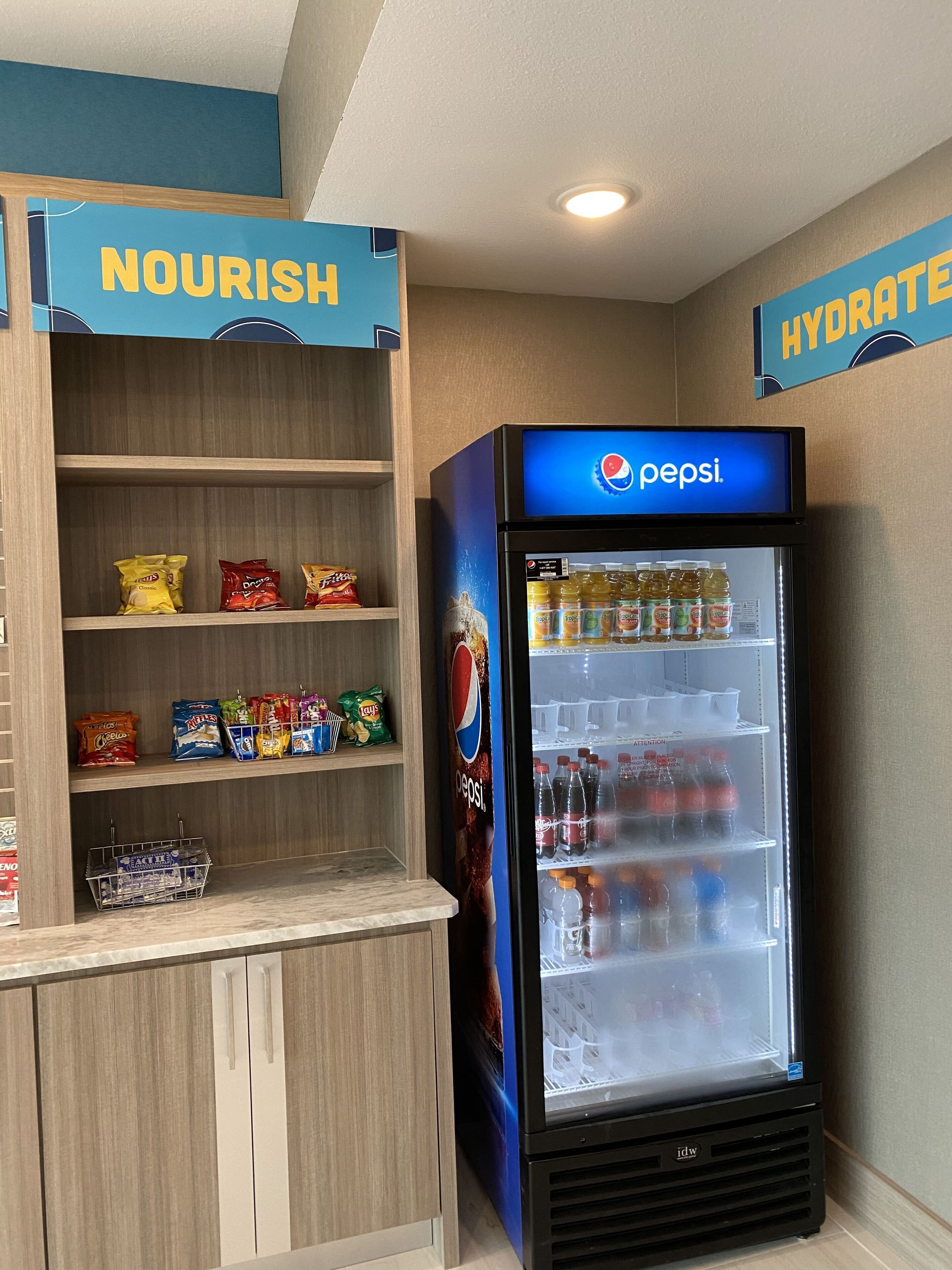 Máquina expendedora llena de bocadillos y bebidas, incluyendo Pepsi, y un estante con varios paquetes de comida.