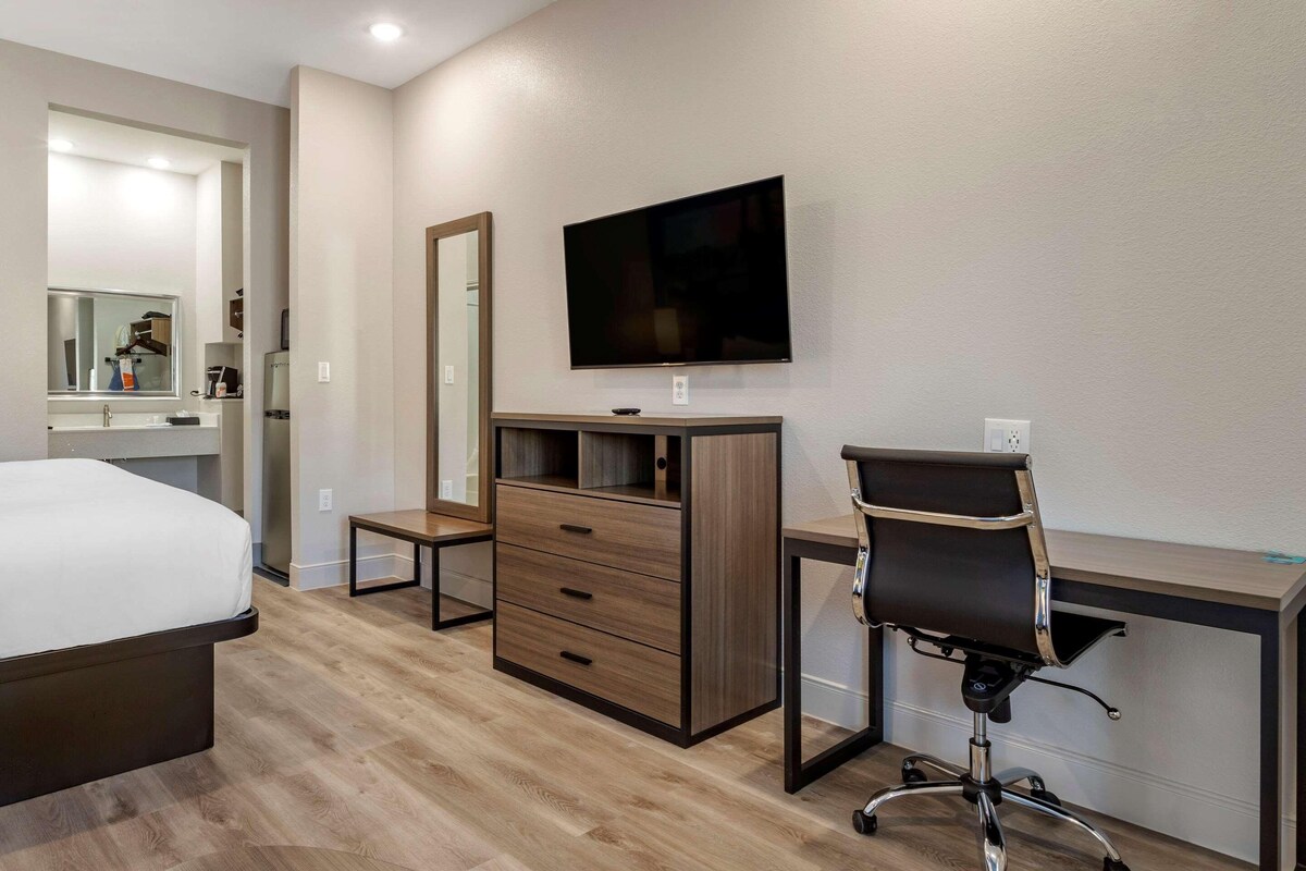 A modern hotel room with a bed, a desk, a chair, a TV, a mirror, and a wardrobe.