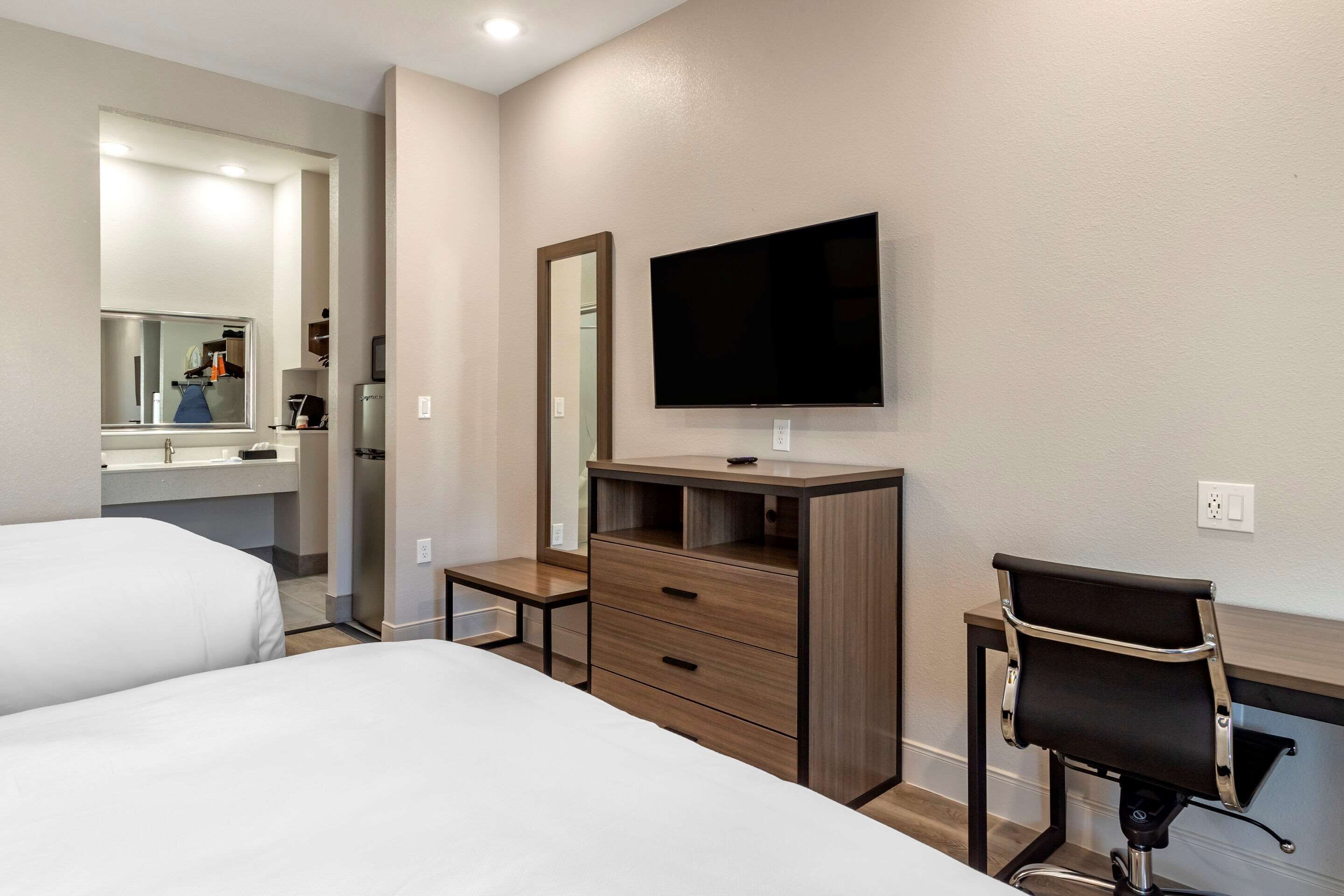 A hotel room with two beds, a desk, a chair, a TV, and a mirror.