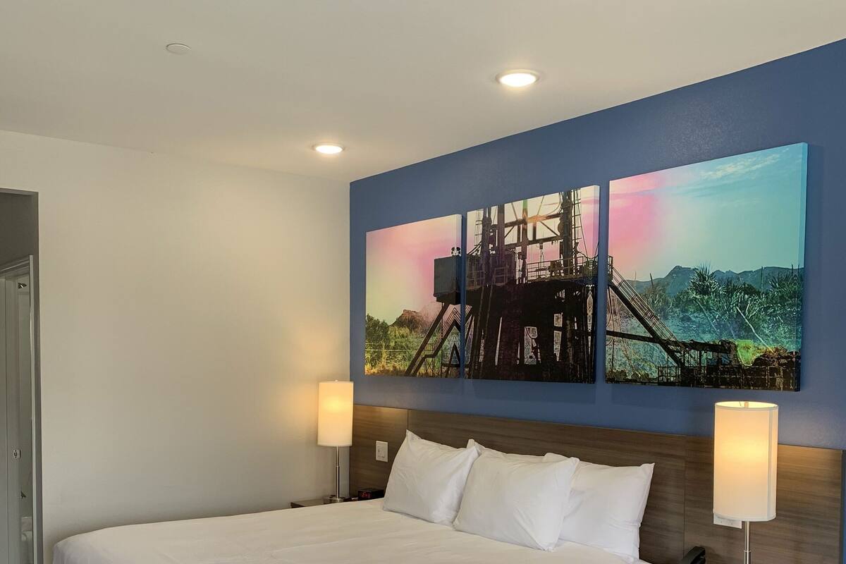 Ein Hotelzimmer mit einem großen Bett, zwei Nachttischlampen, einem Nachttisch und einem Wandbild.