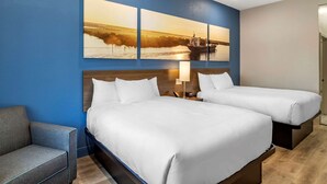 Habitación de hotel con dos camas, un sofá, un cuadro colgado en la pared y una mesita de noche con lámpara.