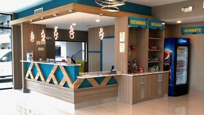 Un área de recepción moderna con un mostrador, un refrigerador de Pepsi y letreros que dicen 'RECHARGE', 'NOURISH' y 'HYDRATE'.