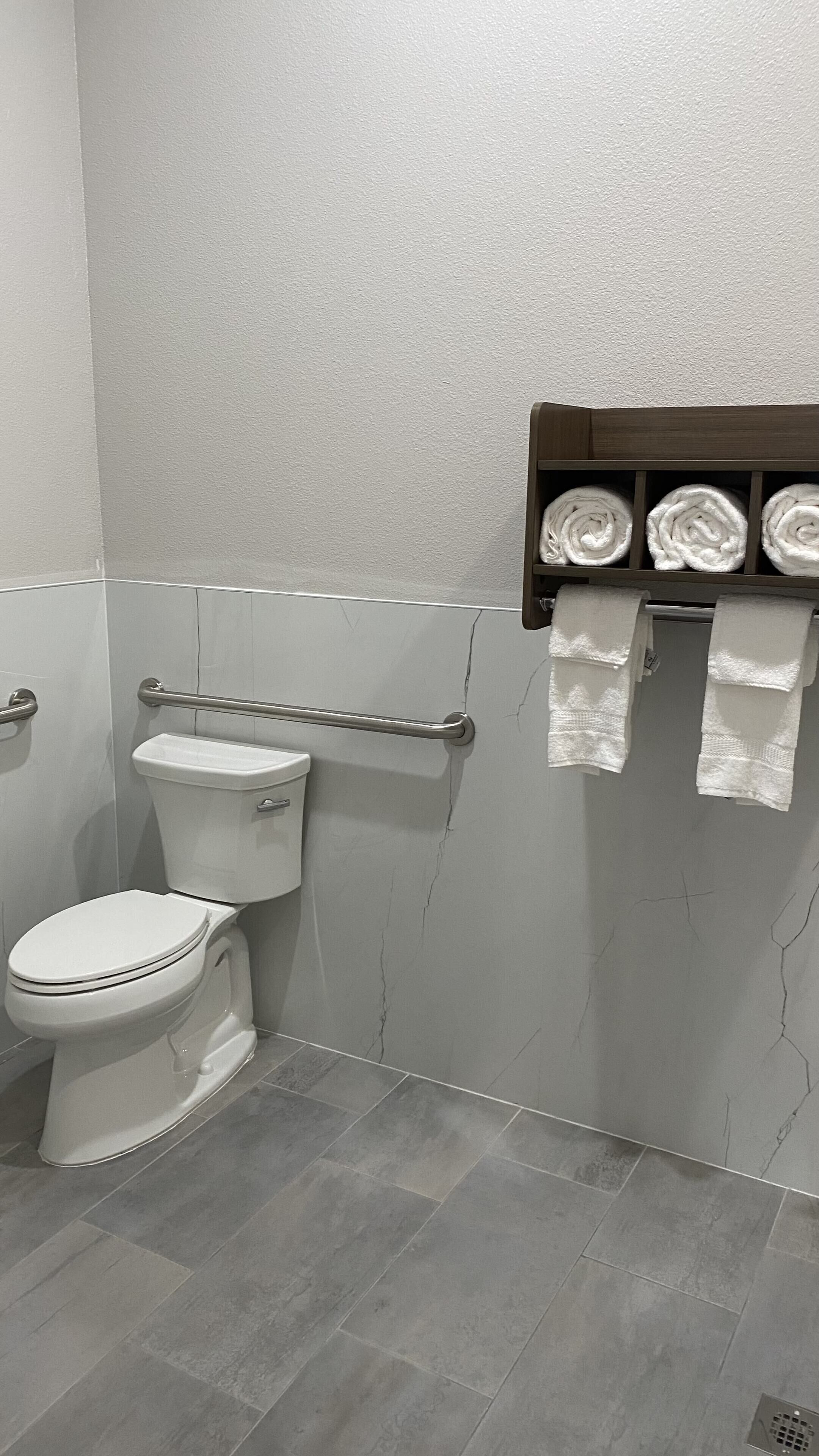 A bathroom with a toilet, a towel rack with towels, and a marble-patterned wall.
