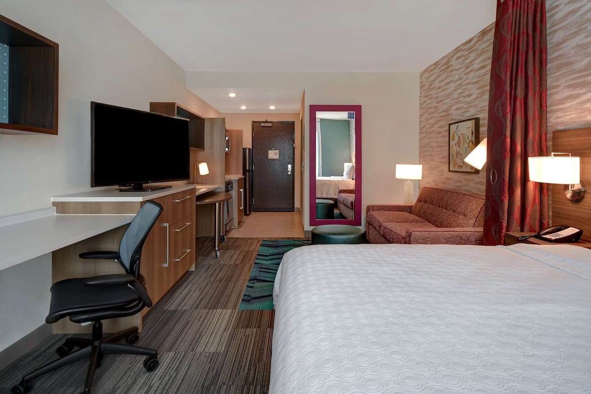 Una habitación de hotel con cama, escritorio, silla, televisor y baño visible a través de una puerta abierta.