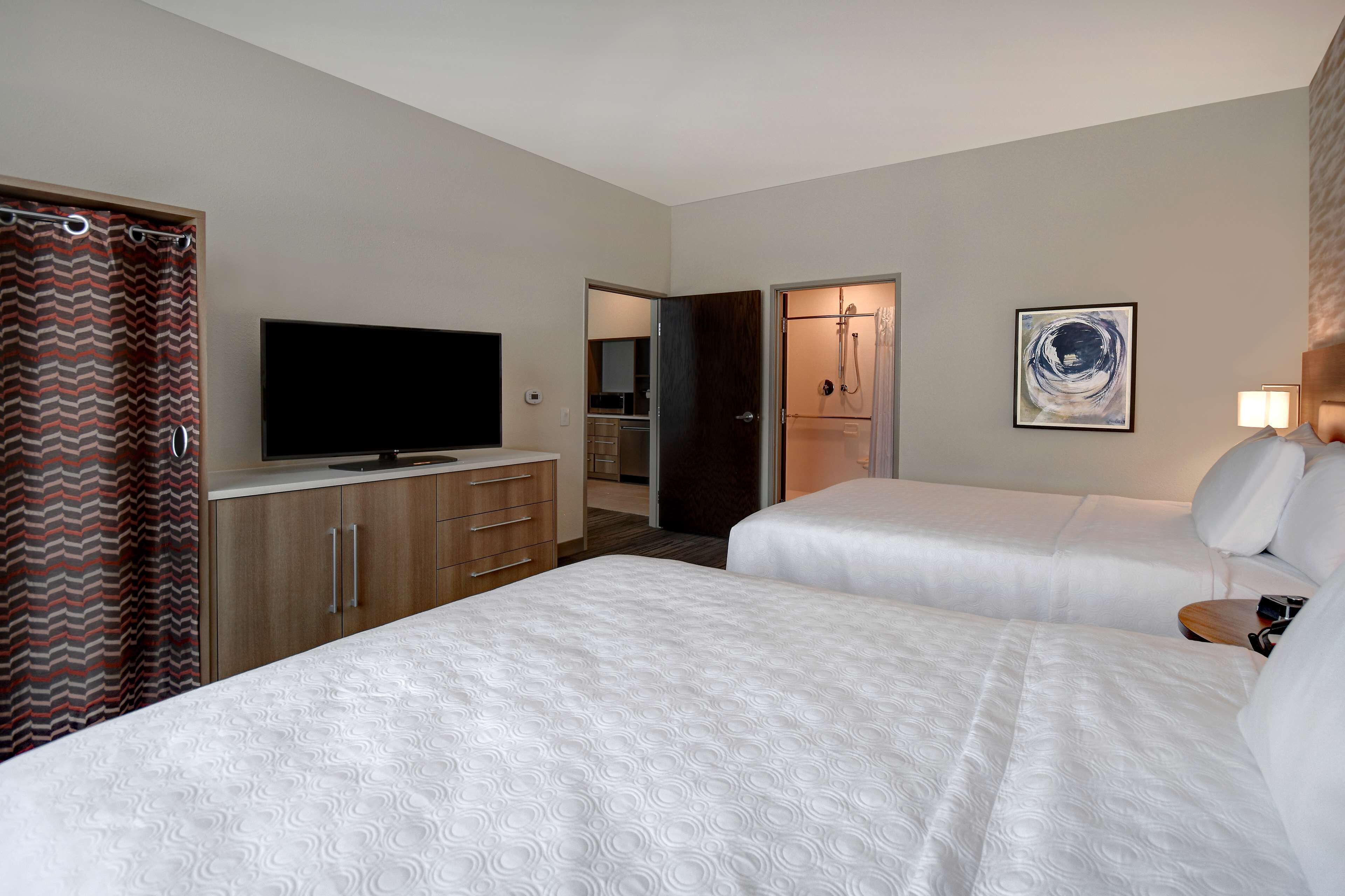 Une chambre d’hôtel avec deux lits, une télévision, un espace douche et un tableau au mur.