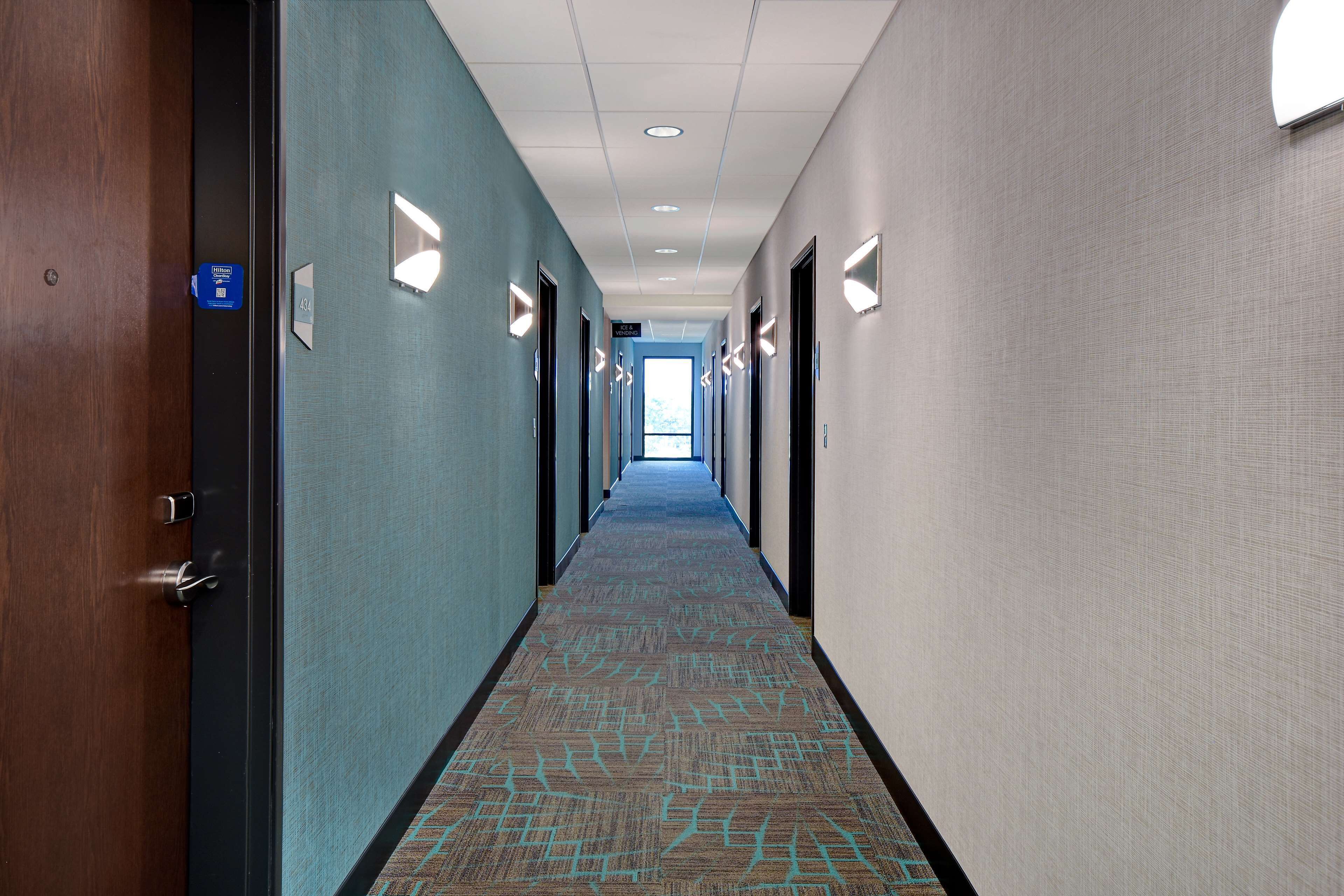 A hotel hallway with carpeted floors, wooden doors, and light-colored walls.