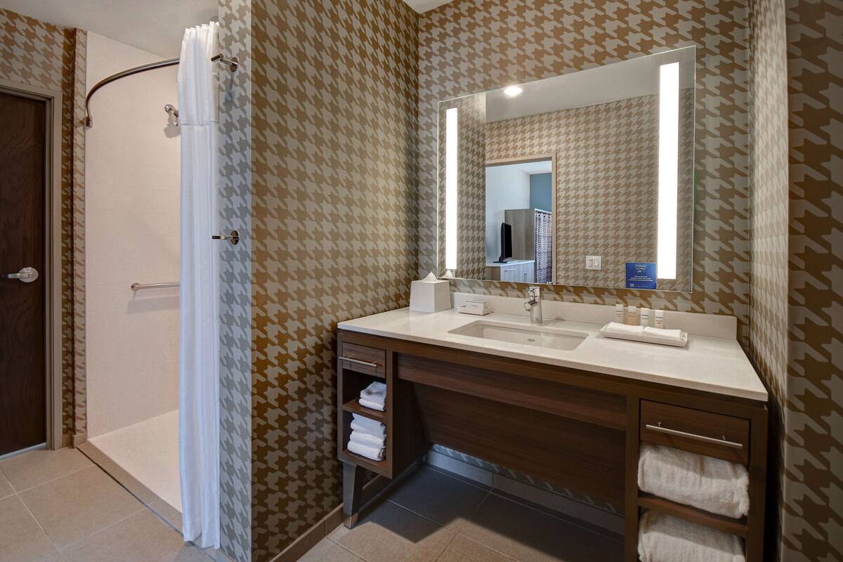 Un baño con ducha, un lavabo con espejo y papel tapiz estampado.