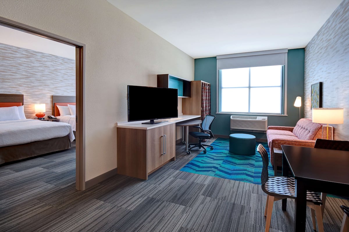 Habitación de hotel con cama, escritorio, televisor y zona de estar.