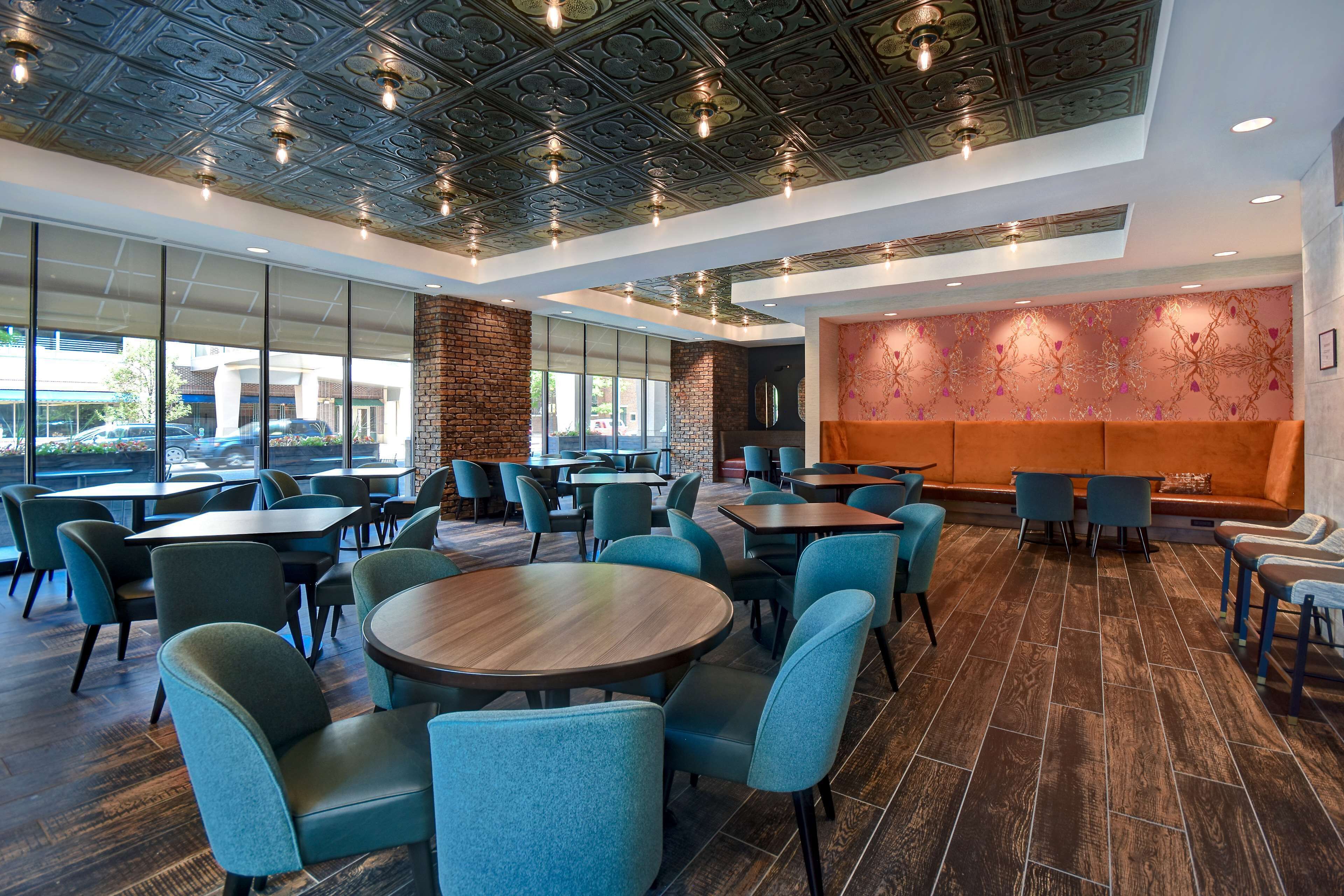 A spacious indoor area with multiple tables and chairs, large windows, and a decorative wall.