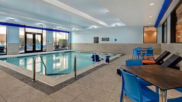 An indoor swimming pool with clear water, a lifeguard chair, and a seating area with blue chairs and a table.