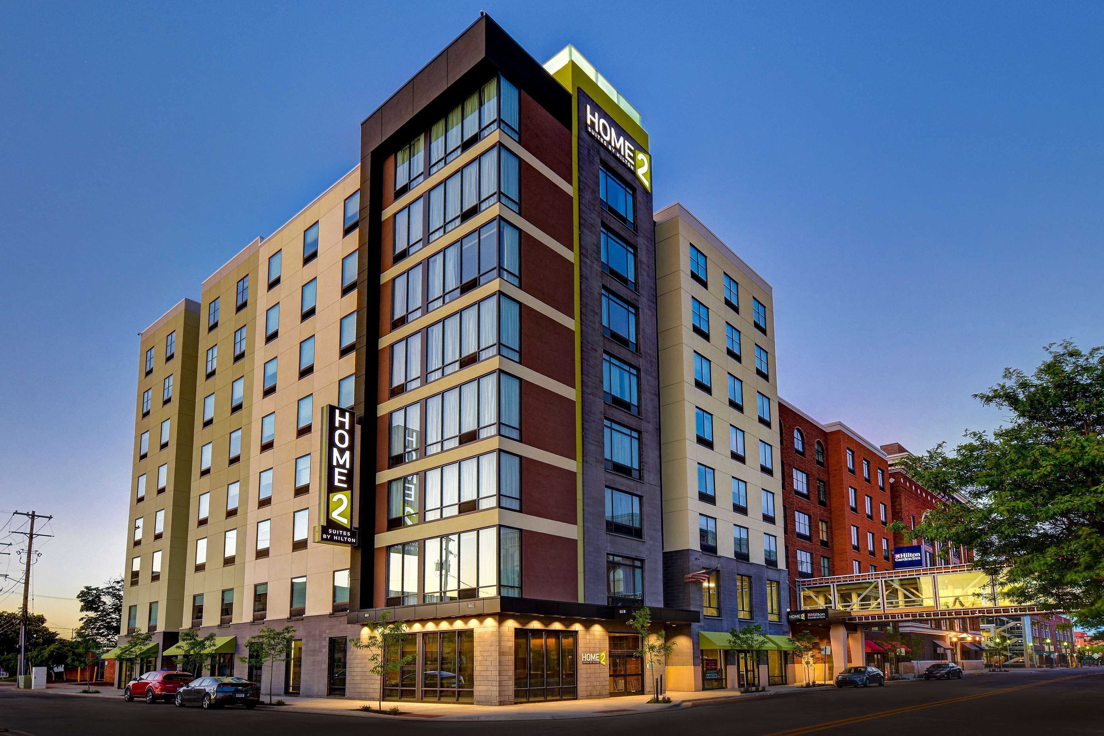 Un hotel de varios pisos con un llamativo letrero de "HOME 2", ventanas amplias y un diseño arquitectónico moderno.