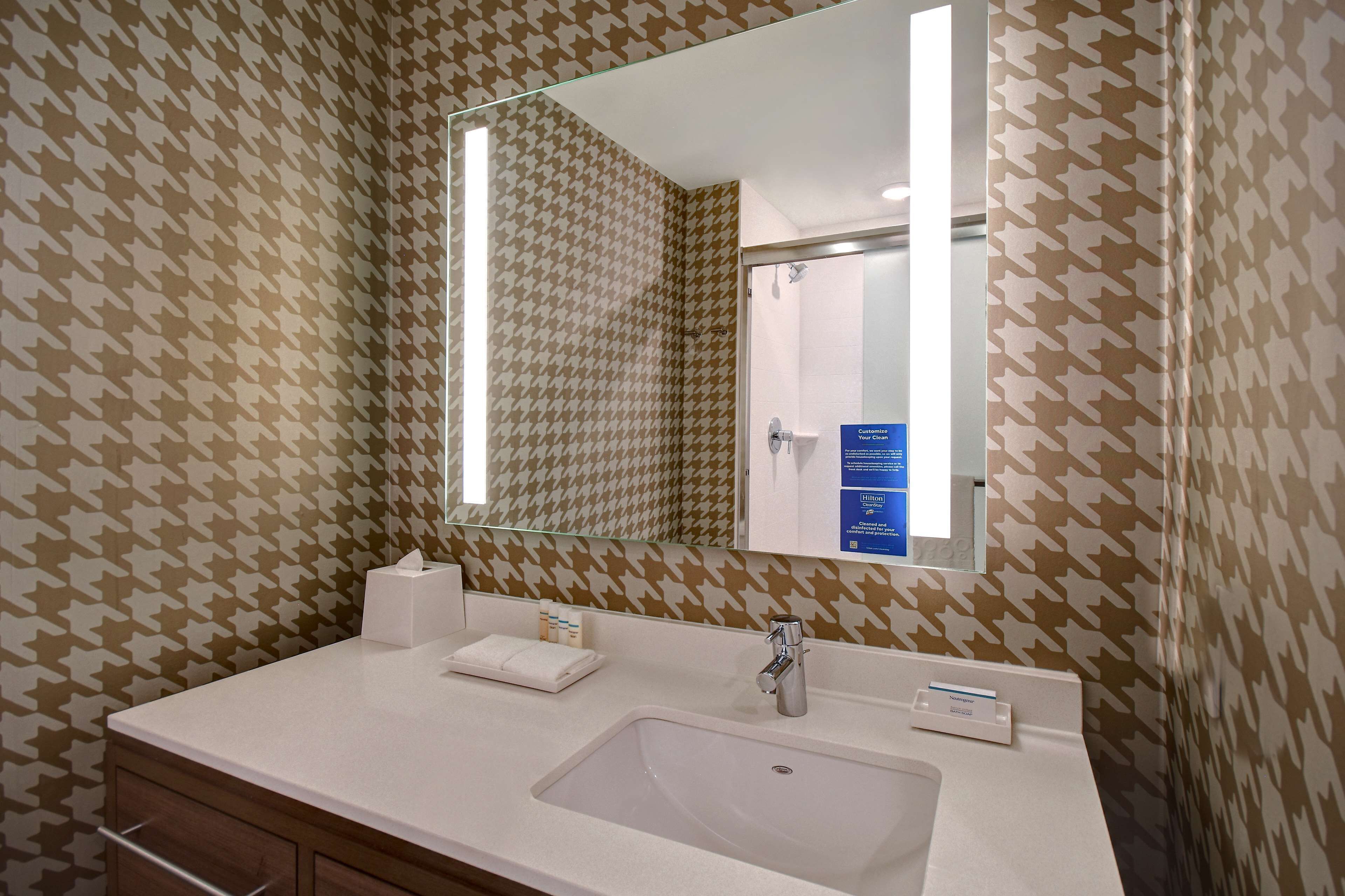 A bathroom with a houndstooth patterned wall, a white sink, a mirror, and a glass shower enclosure.