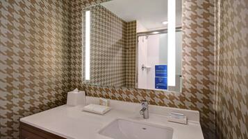 A bathroom with a houndstooth patterned wall, a white sink, a mirror, and a glass shower enclosure.