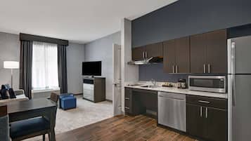 A modern kitchen with dark cabinets, stainless steel appliances, and a flat-screen TV.