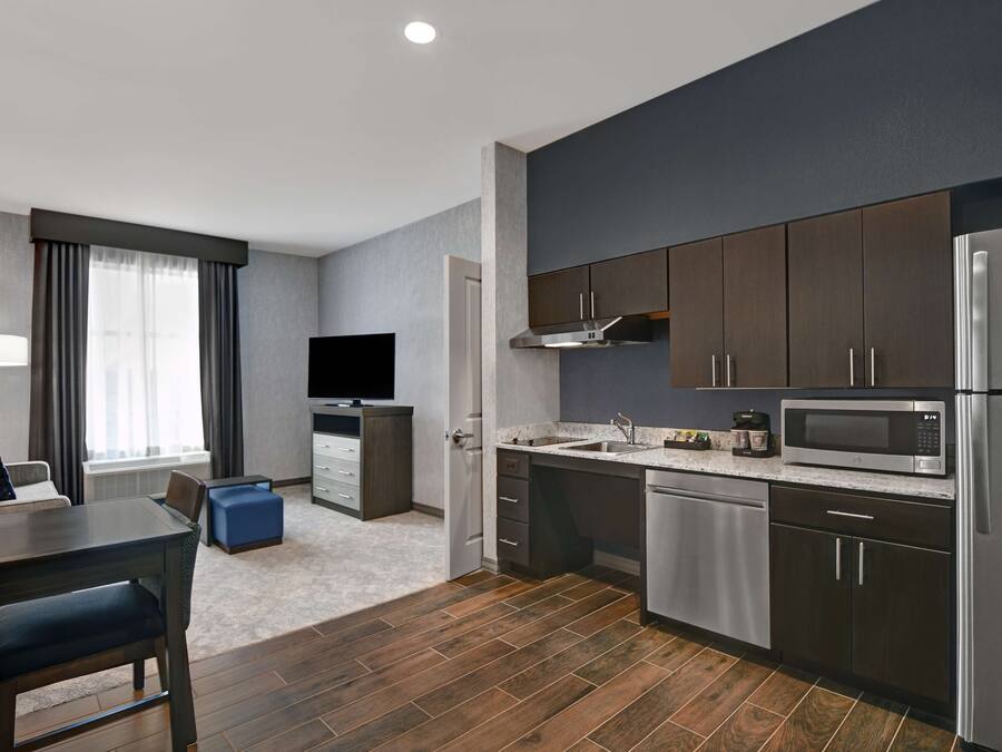 A modern kitchen with dark cabinets, stainless steel appliances, and a flat-screen TV.