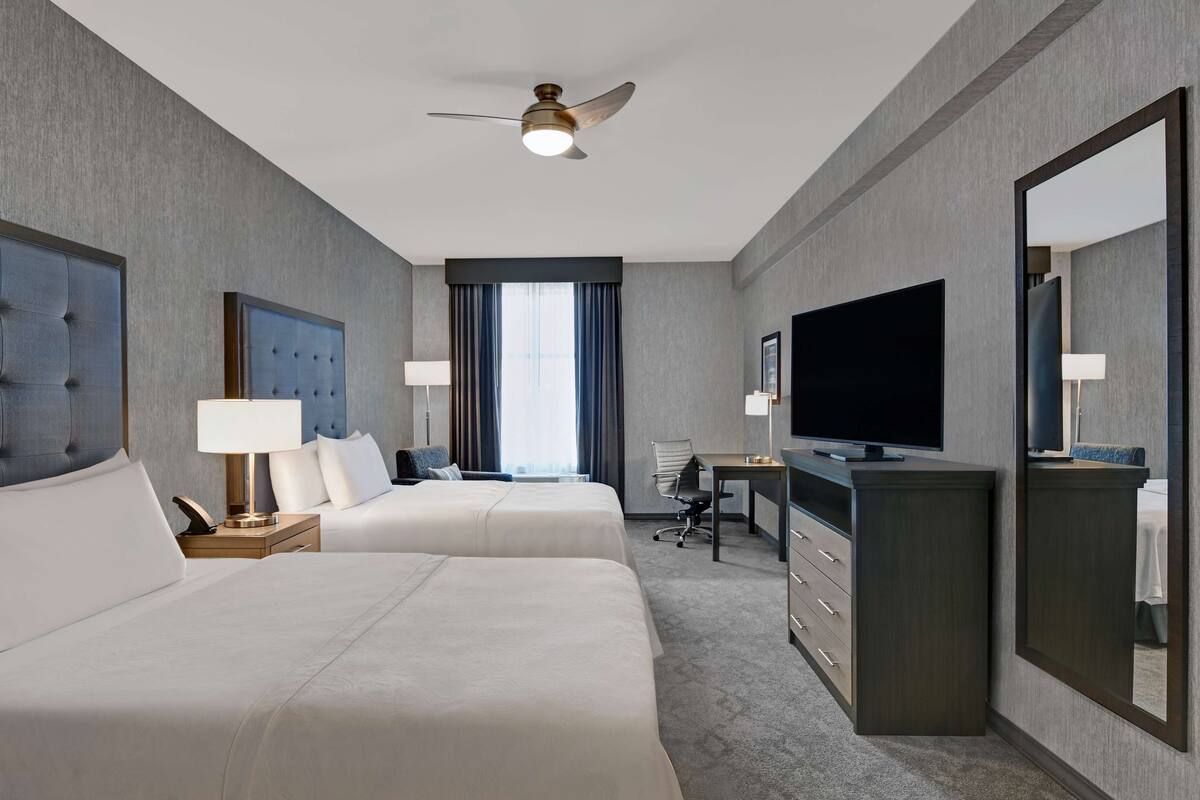 Une chambre d’hôtel avec deux lits, un bureau, une télévision et un ventilateur de plafond.