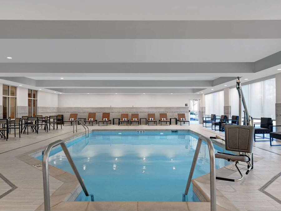 An indoor swimming pool with clear water, surrounded by lounge chairs and a seating area with tables.