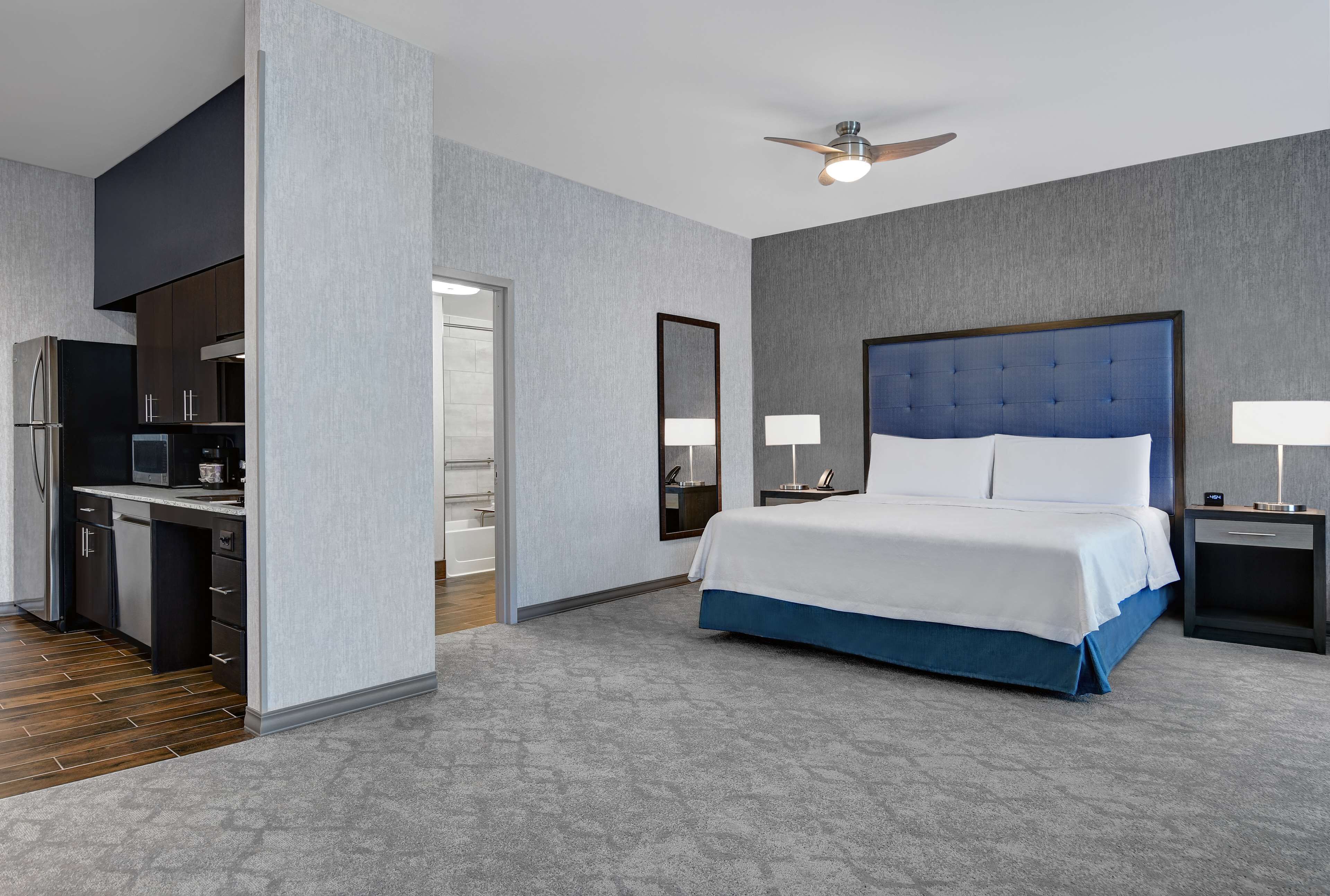 A modern hotel room with a large bed, a desk, and a kitchenette.