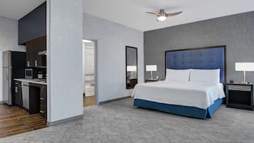 A modern hotel room with a large bed, a desk, and a kitchenette.
