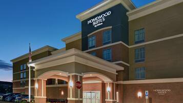 A hotel with a prominent "Homewood Suites by Hilton" sign, a stop sign, and a parking lot with cars.