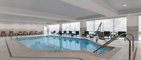 A large indoor swimming pool with clear water, surrounded by lounge chairs and a sun terrace.