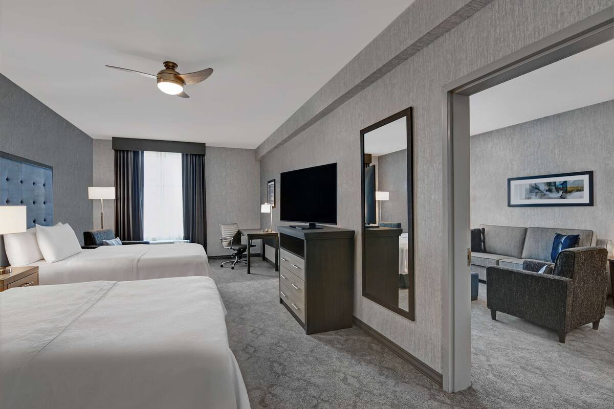 Une chambre d ’hôtel avec deux lits, un bureau, une télévision, un miroir, un canapé et un ventilateur de plafond.