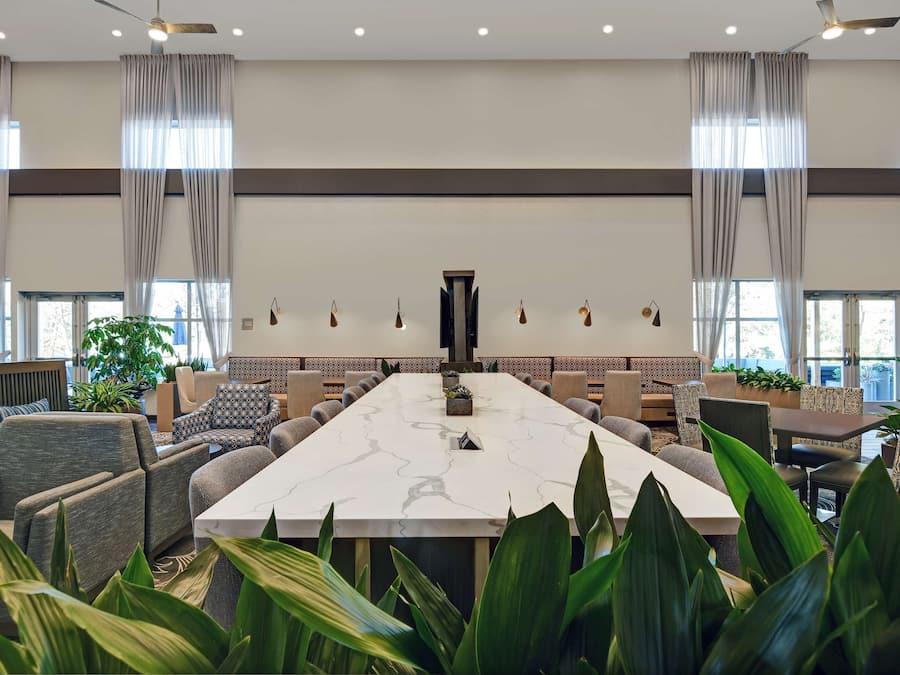Ein geräumiger Konferenzraum mit einem großen Marmortisch, bequemen Sitzgelegenheiten und großen Fenstern mit Vorhängen.