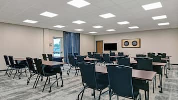 Ein Konferenzraum mit mehreren Tischen und Stühlen, einer großen Leinwand und einer Tür mit Blick.