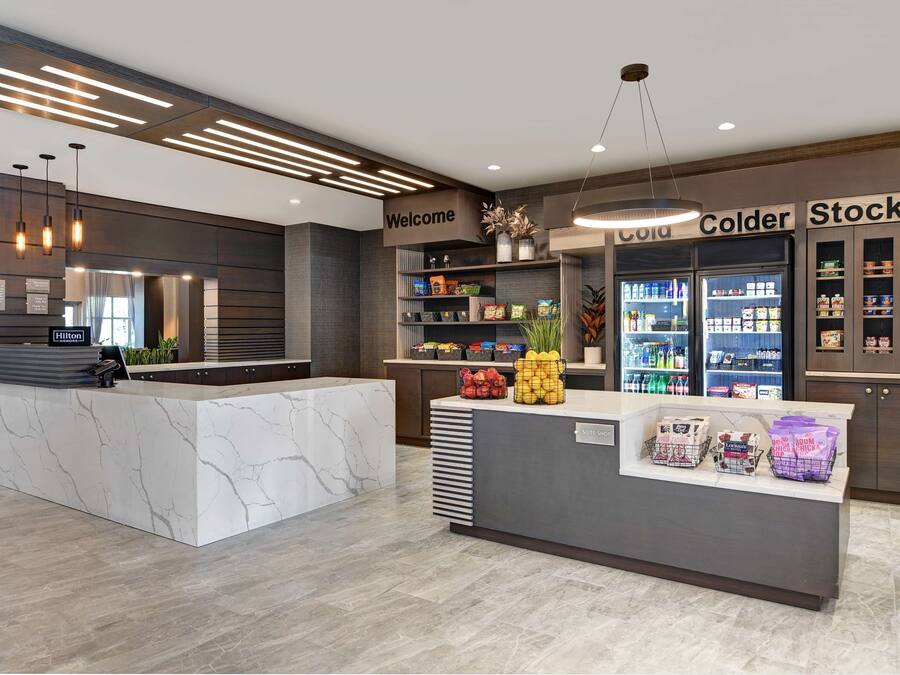 A hotel reception area with a marble counter, a 'Welcome' sign, a 'Cold' and 'Stock Up' refrigerator, and a 'Suite' label on the counter.