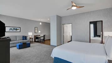 A hotel room with a large bed, a desk, a sofa, and a ceiling fan.