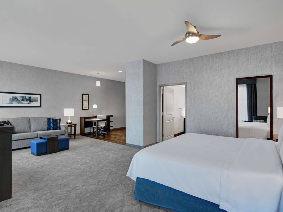 A hotel room with a large bed, a desk, a sofa, and a ceiling fan.