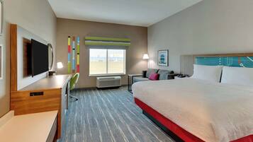 A hotel room with a large bed, a desk with a flat-screen TV, a chair, a window with a view, and a lamp.