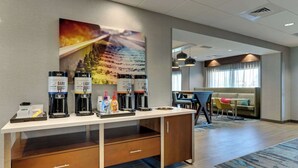 Un espace d’accueil d’hôtel comprenant un coin café, un tableau accroché au mur et un espace détente avec un canapé et des fauteuils.