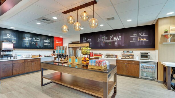 Un espace cuisine moderne doté d’un îlot central, de luminaires suspendus et d’un mur noir où sont dessinés des motifs et écrits des textes sur le thème de la cuisine.