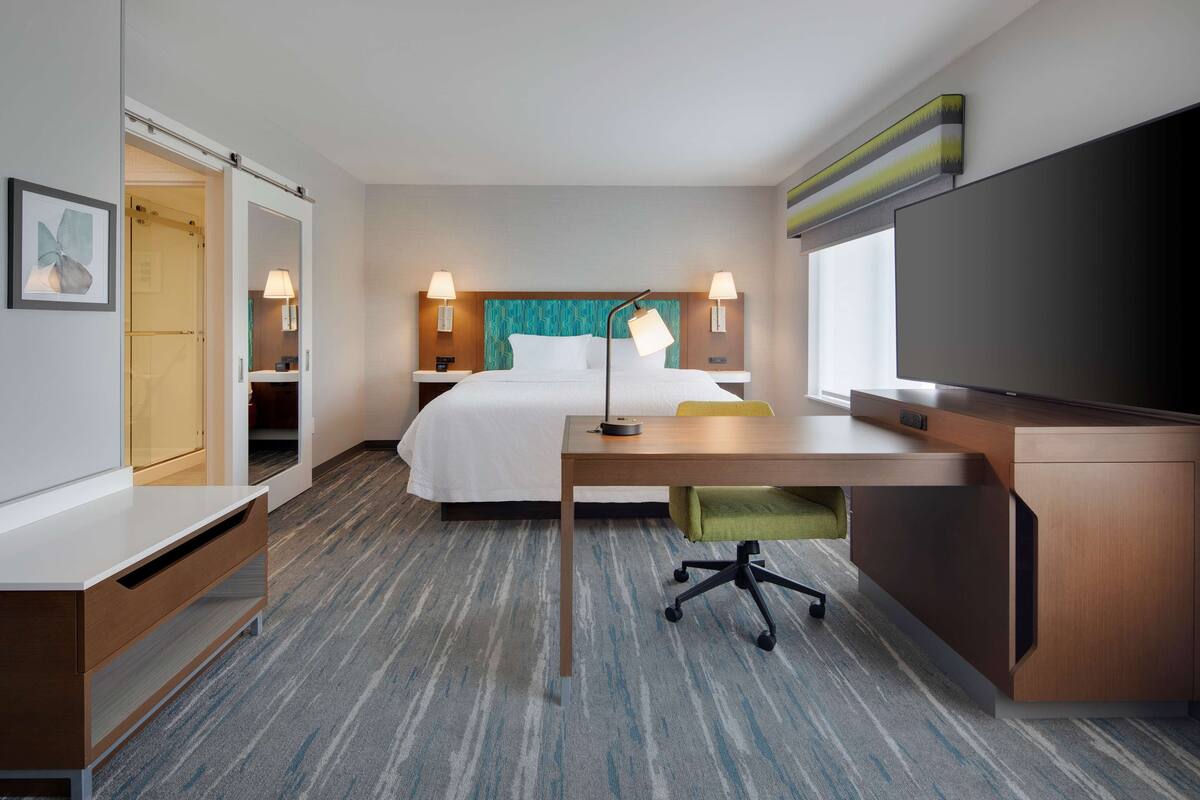 Ein Hotelzimmer mit Bett, Schreibtisch, Stuhl, Fernseher, Nachttischlampen und einem Kleiderschrank.