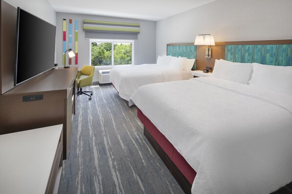 Une chambre d’hôtel avec deux lits, un bureau, une télévision et une fenêtre donnant sur un paysage verdoyant.