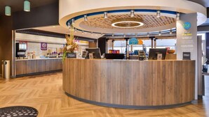 Un moderno mostrador de recepción de hotel con una mesa de madera, una pantalla digital y un mostrador que exhibe servicios.