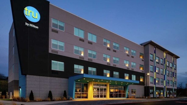 Un moderno edificio de hotel con un llamativo letrero de 'tru by Hilton', varios pisos y una entrada bien iluminada.