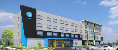 A hotel with a modern design, featuring a prominent logo on the facade, a central entrance, and a parking area with several cars.