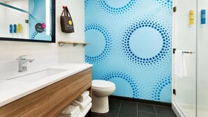 Un baño moderno con un lavamanos blanco, tocador de madera y un inodoro. Hay un espejo sobre el lavamanos y un perchero en la pared.