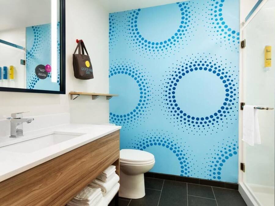 Un baño moderno con un lavamanos blanco, tocador de madera y un inodoro. Hay un espejo sobre el lavamanos y un perchero en la pared.