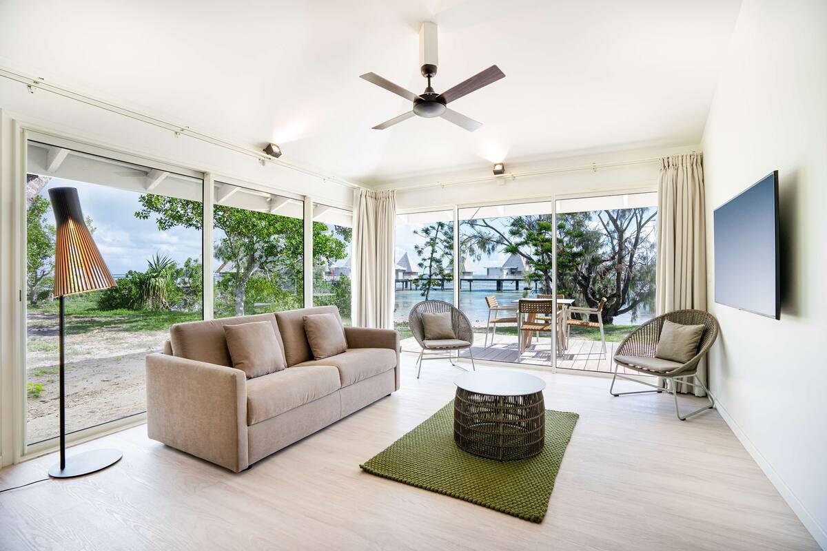A modern living room with a beige sofa, a round coffee table, wicker chairs, and a ceiling fan.