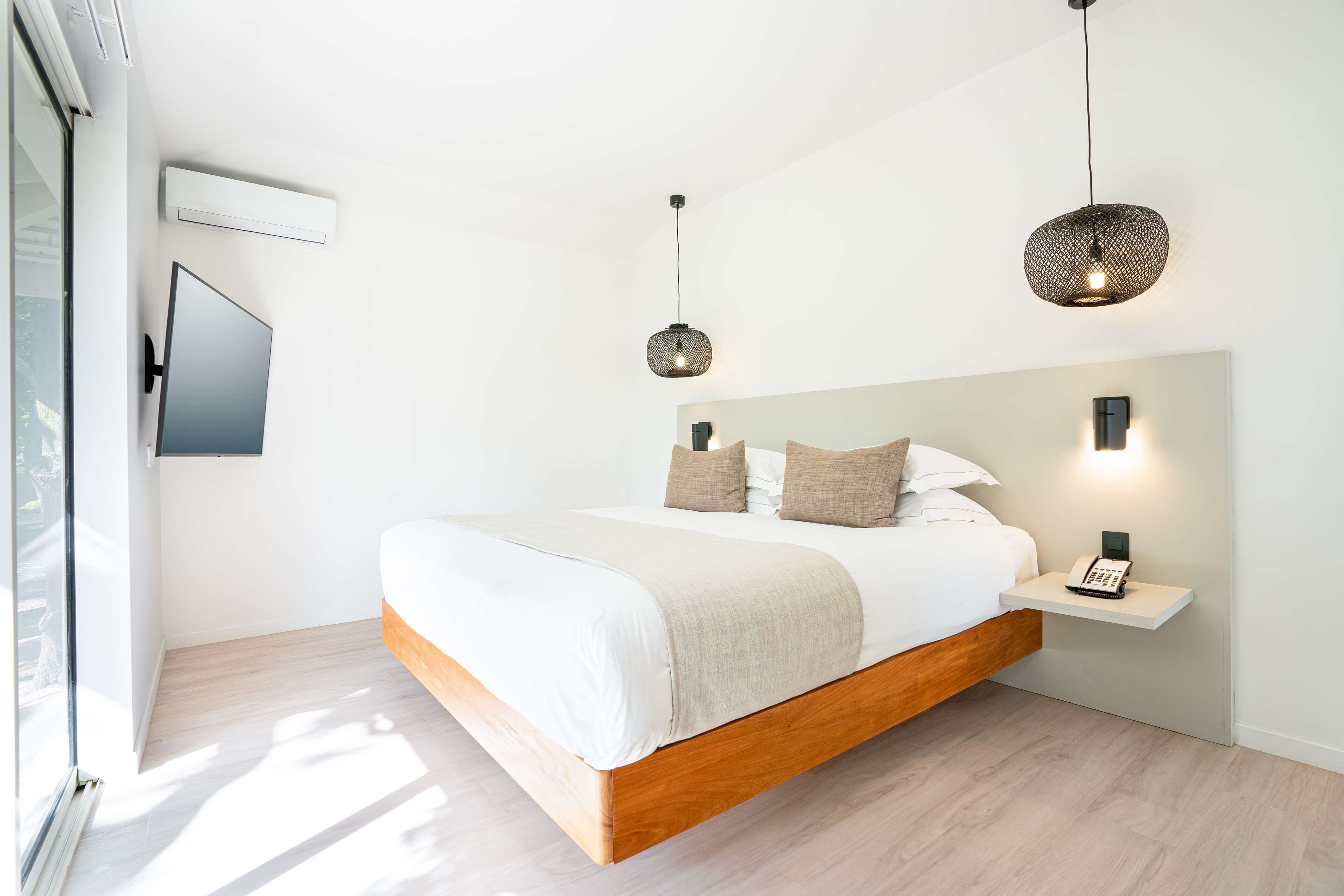 A modern bedroom with a wooden bed, a bedside phone, and a wall-mounted TV.