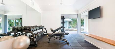 Un gimnasio con equipo de ejercicio, televisión y ventanas amplias.